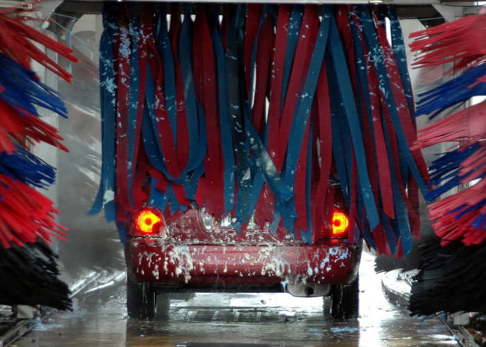 En bil rör sig genom en automatisk biltvätt, dess bakre bromsljus är upplysta, omgiven av svajande blå och röda borstar.