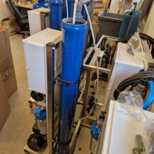 Laboratorieuppsättning med olika utrustning inklusive pumpar, slangar och en blå cylindrisk behållare, med lådor och verktyg utspridda.