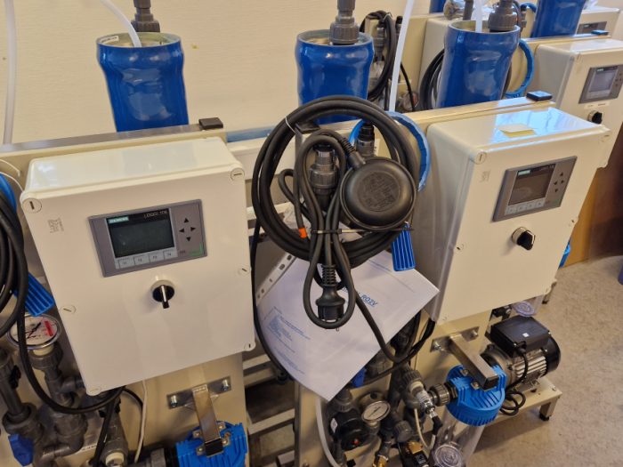 Flera industriella vattenpumpar och styrenheter på en laboratoriebänk, utrustade med digitala displayer och sammankopplade med olika kablar och rör.